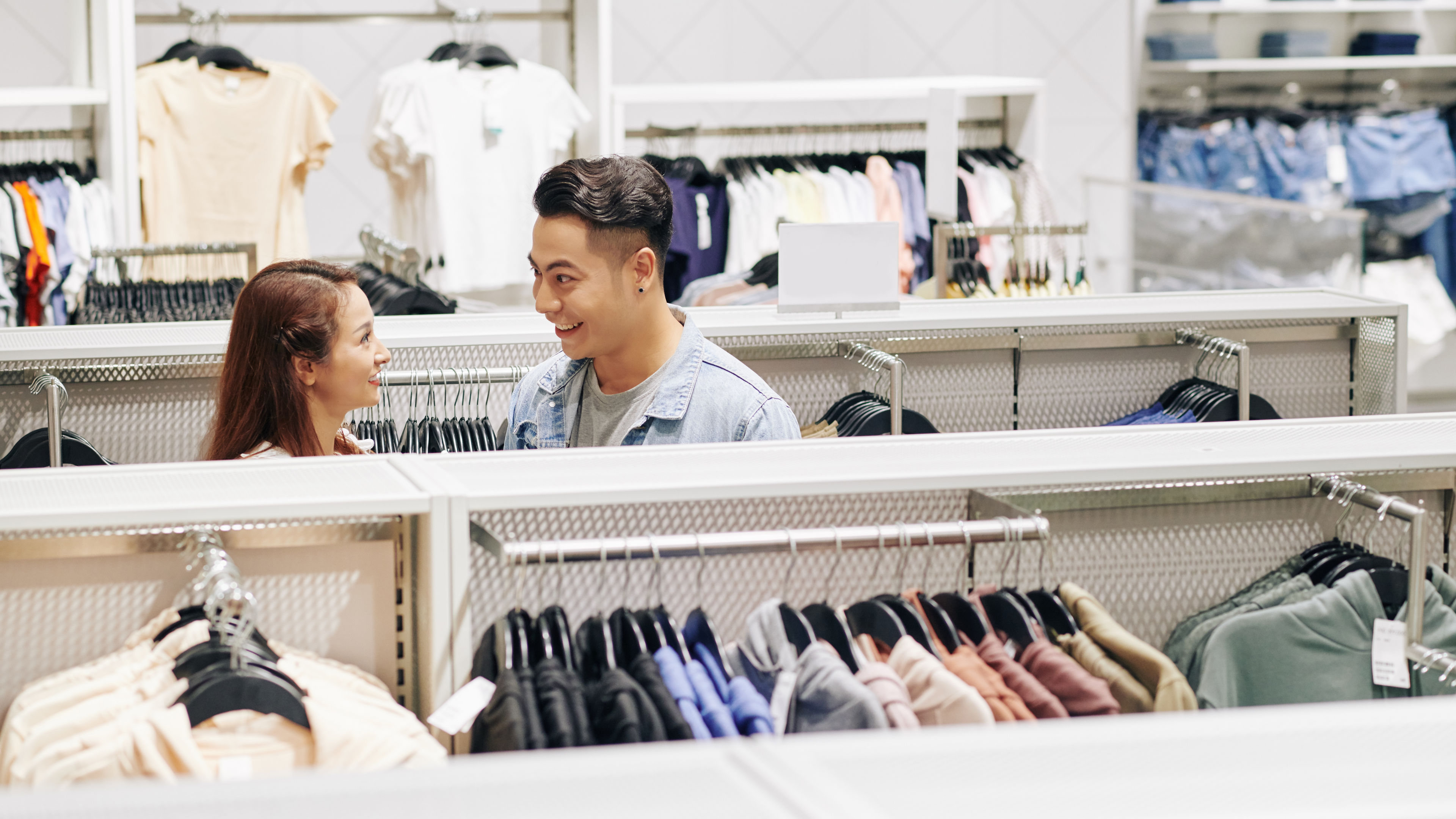 Asian couple shopping for clothes in a store, browsing through clothing racks.