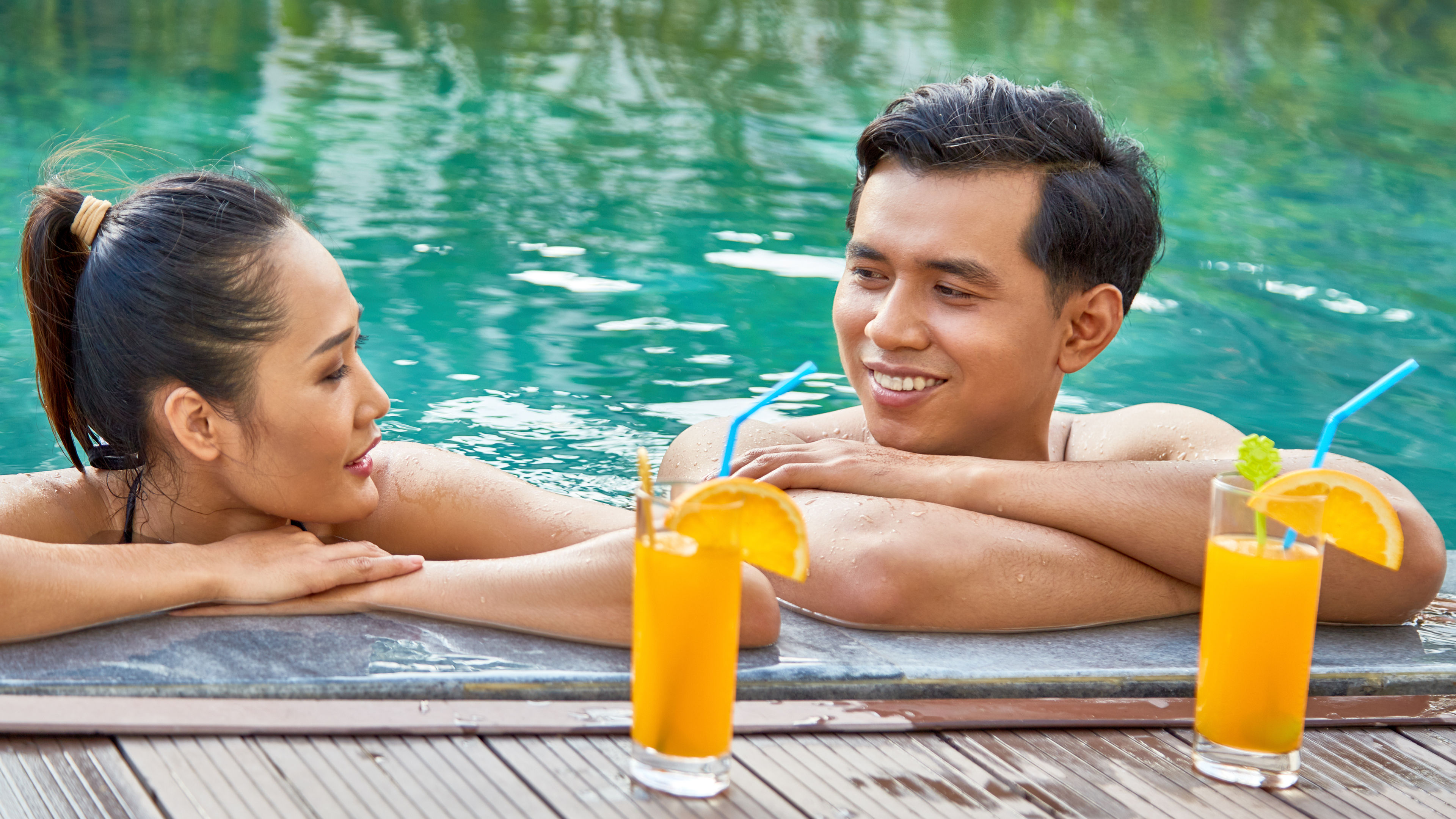 Happy Asian couple nakakarelaks at paglangoy sa isang pool sa isang maaraw na araw.