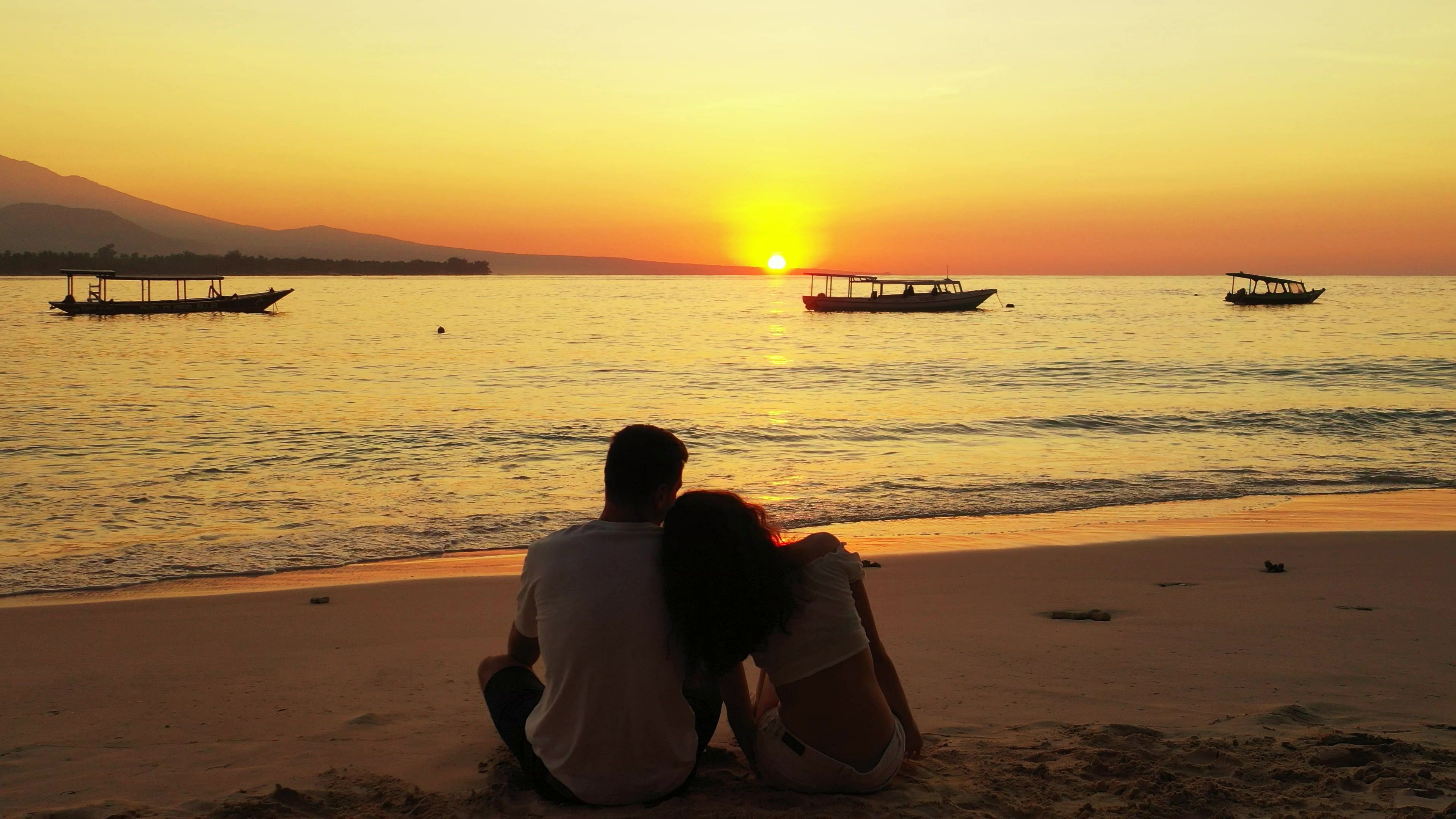 A couple is sitting on a sandy beach