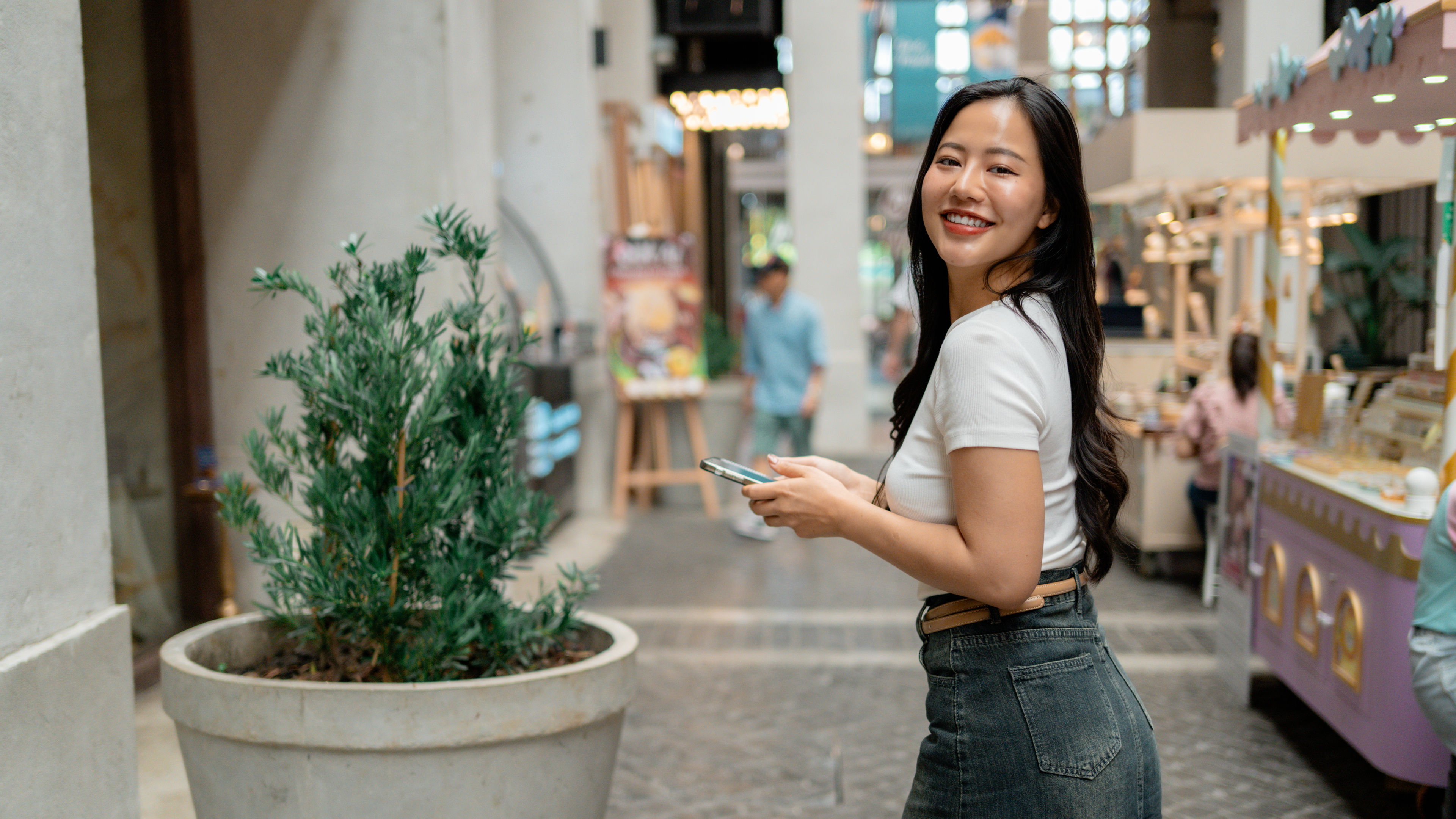 A smiling young woman is walking in an open shopping area