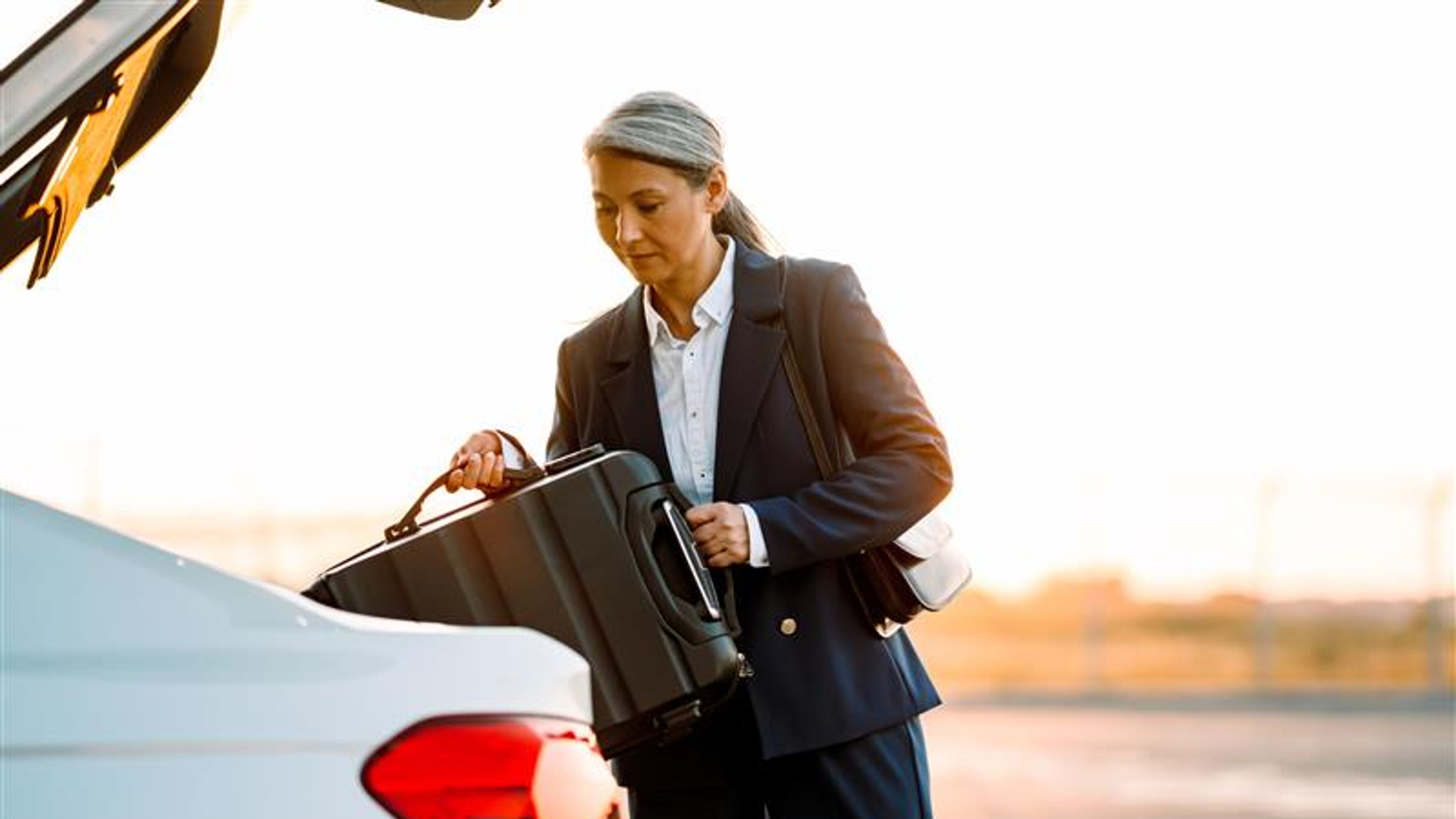 A woman is putting her suitcase in the car