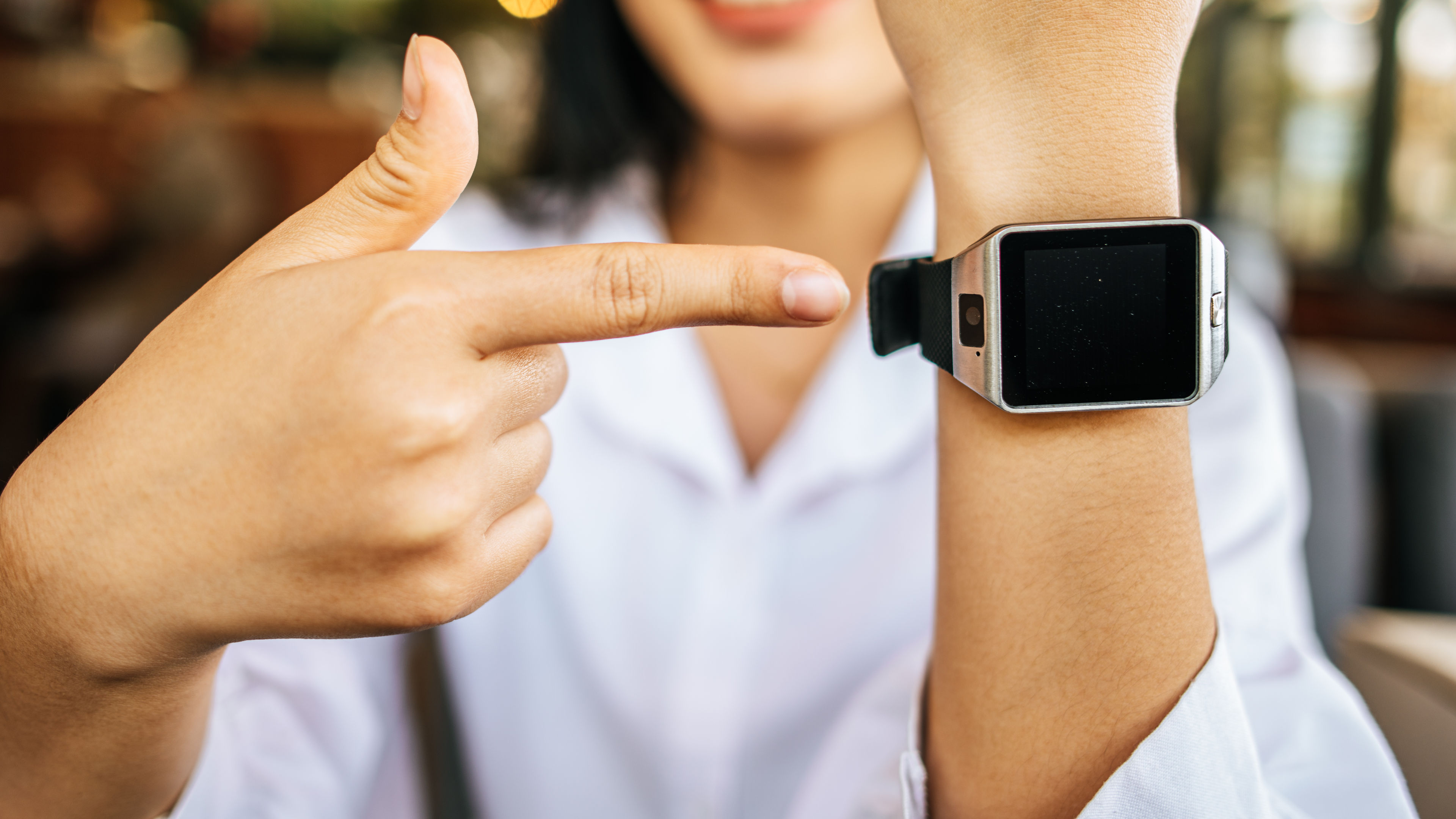 A smartwatch on the wrist with a right hand pointing at it. 

 