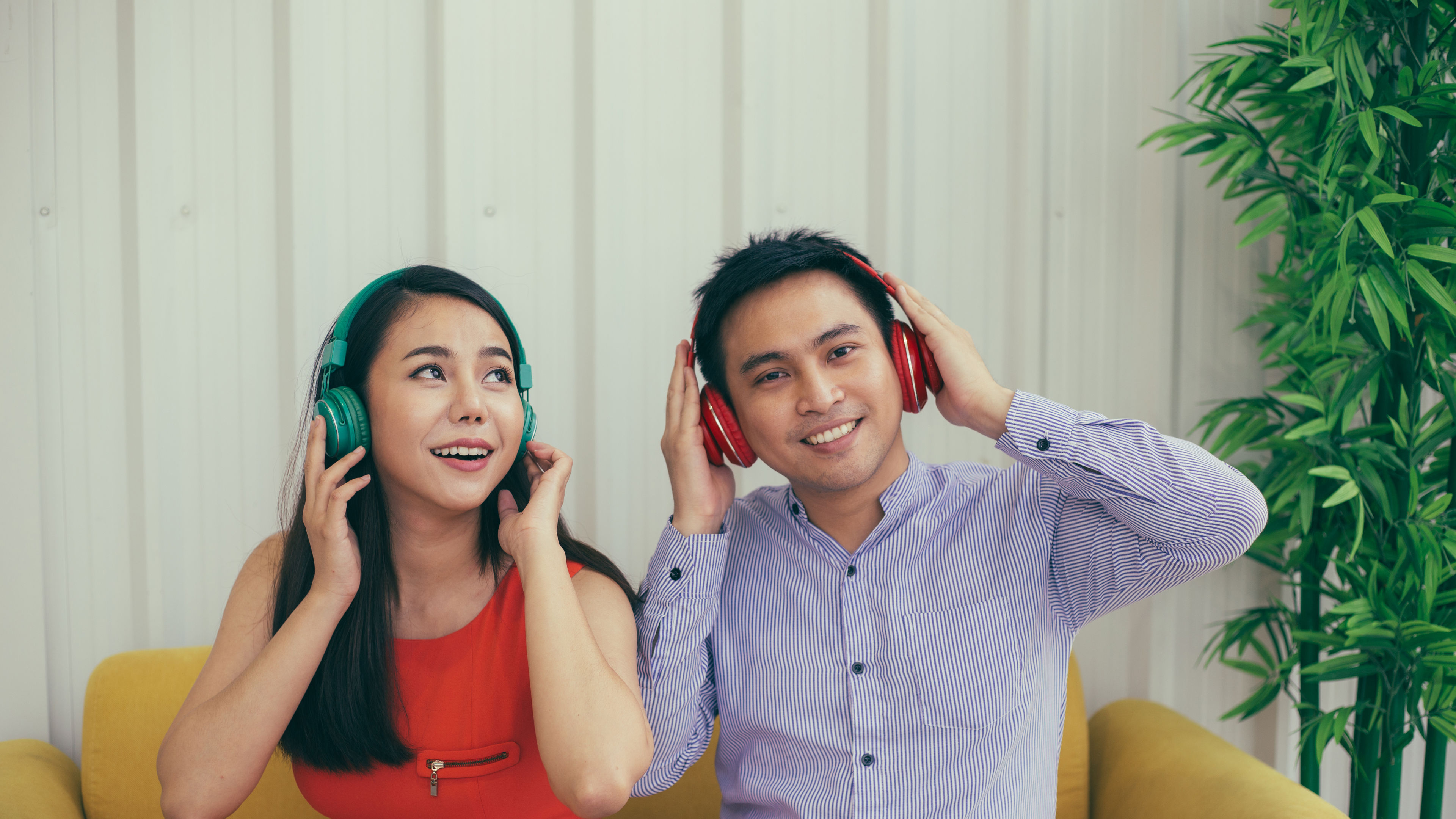 A couple sits closely, sharing headphones and smiling as they enjoy music together.