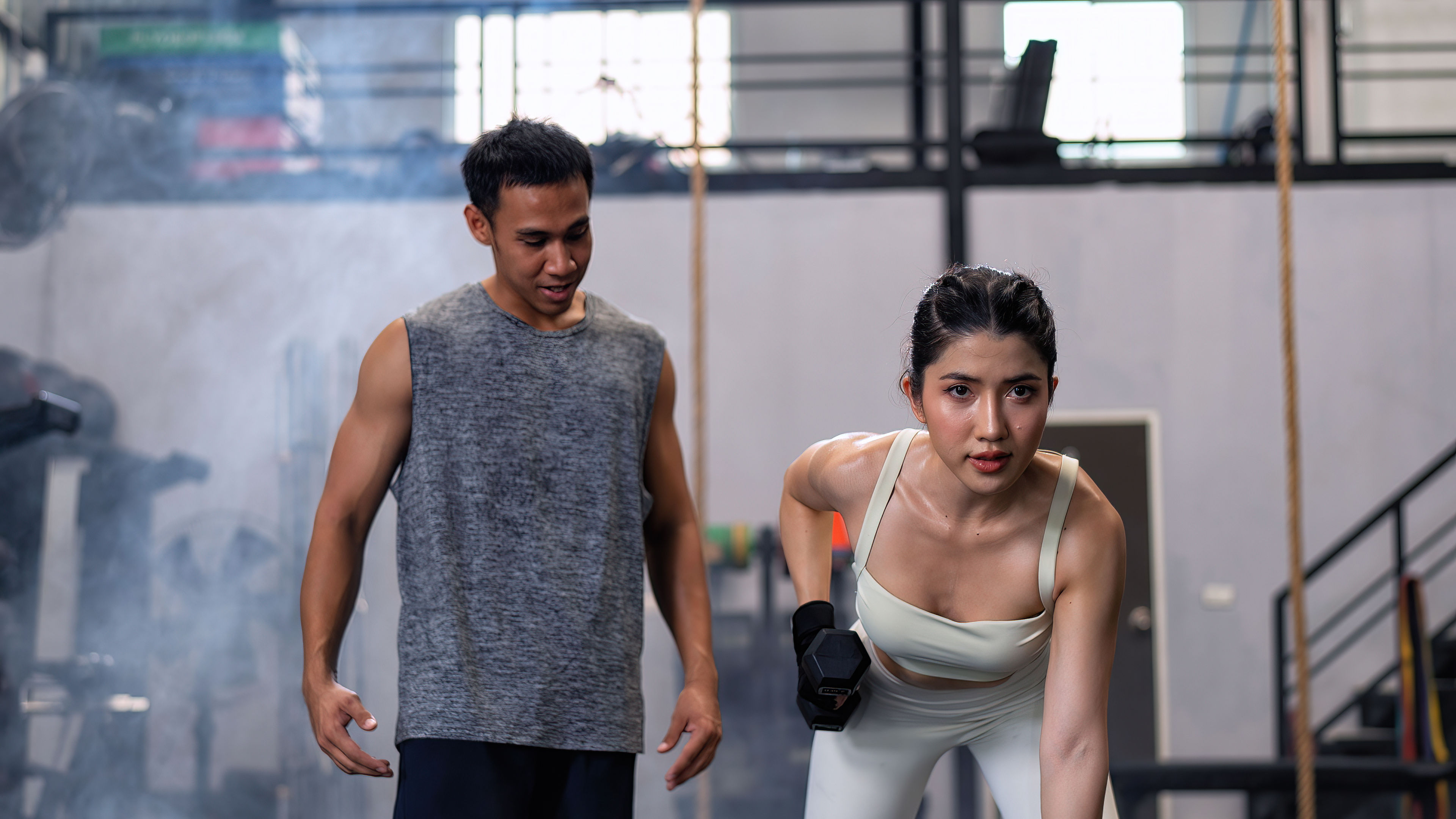 Male fitness center instructor help woman lifting dumbbell workout at fitness center