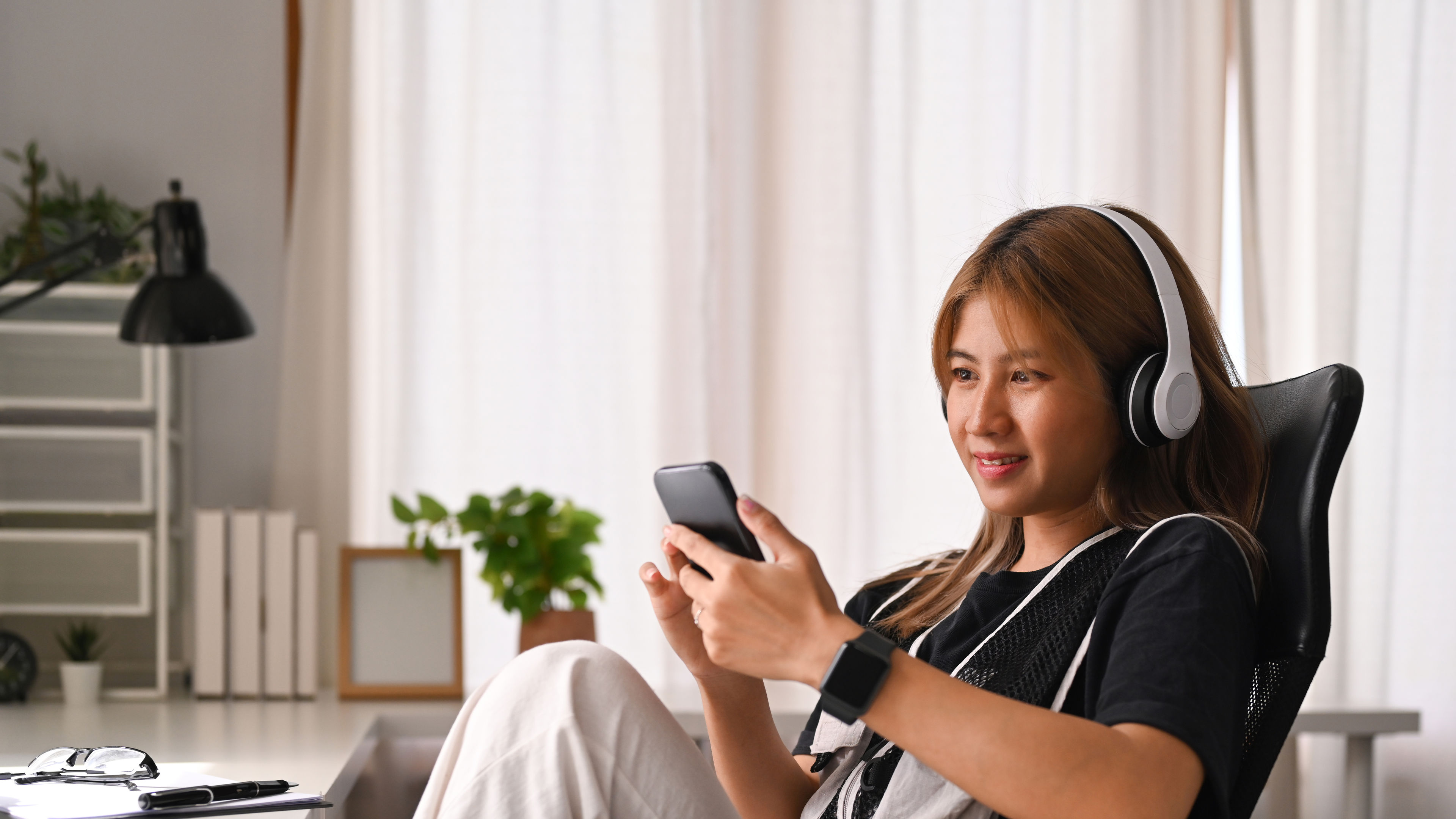 Smiling young woman sitting on office chair and using mobile phone