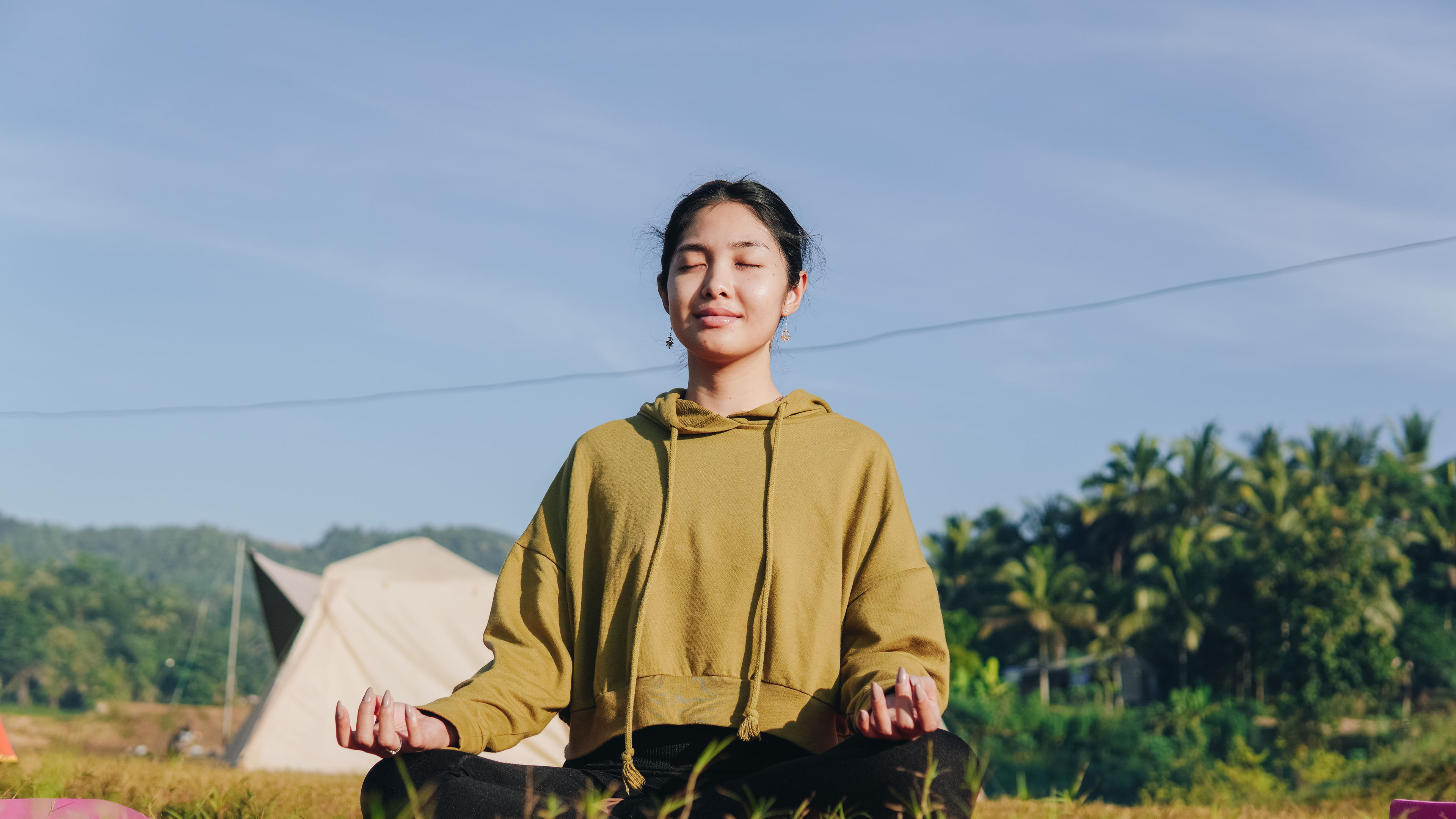 Woman is sitting in a field, wearing a green hoodie and doing yoga