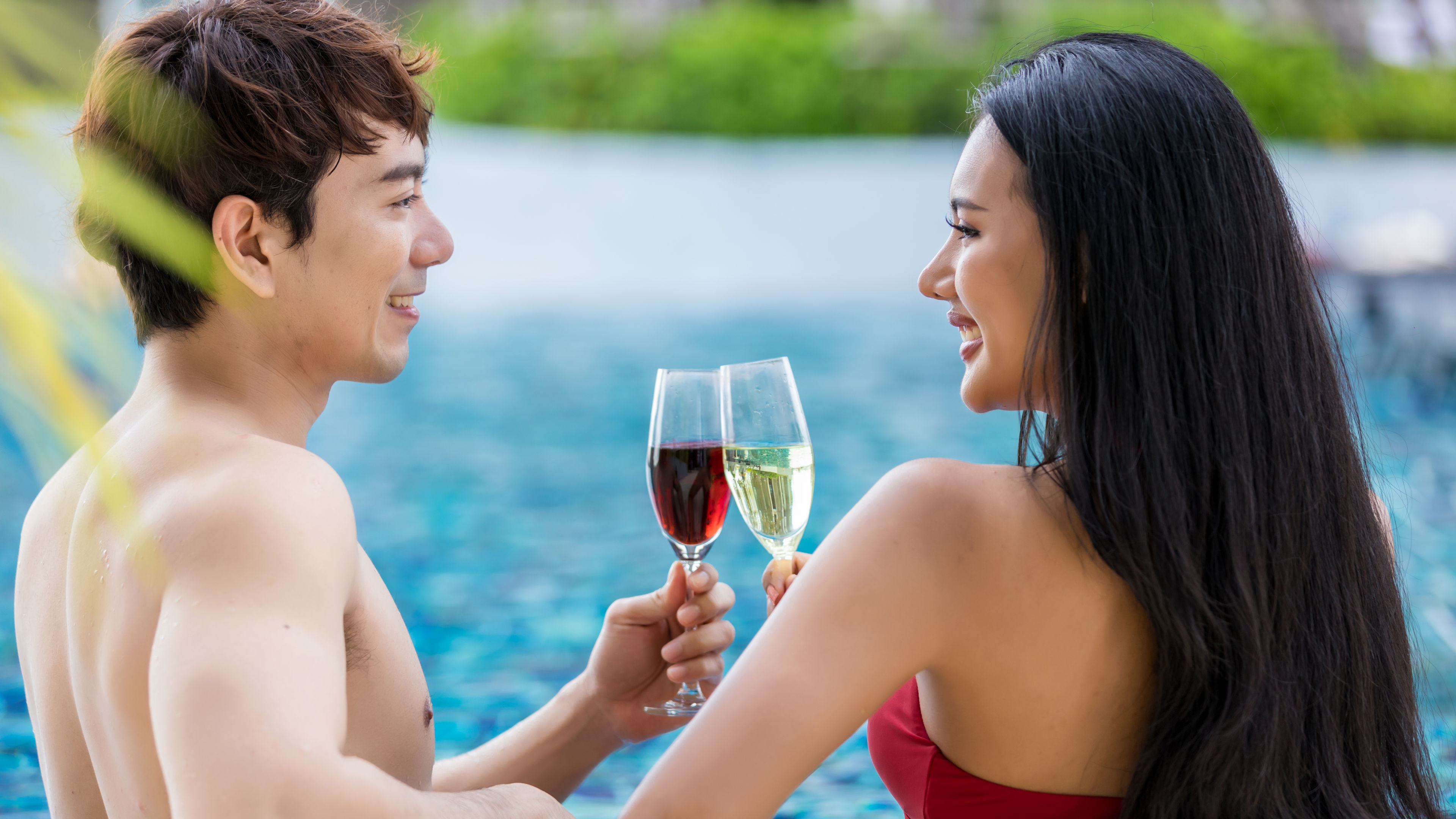 A young Asian couple enjoys red and golden champagne by the pool. 